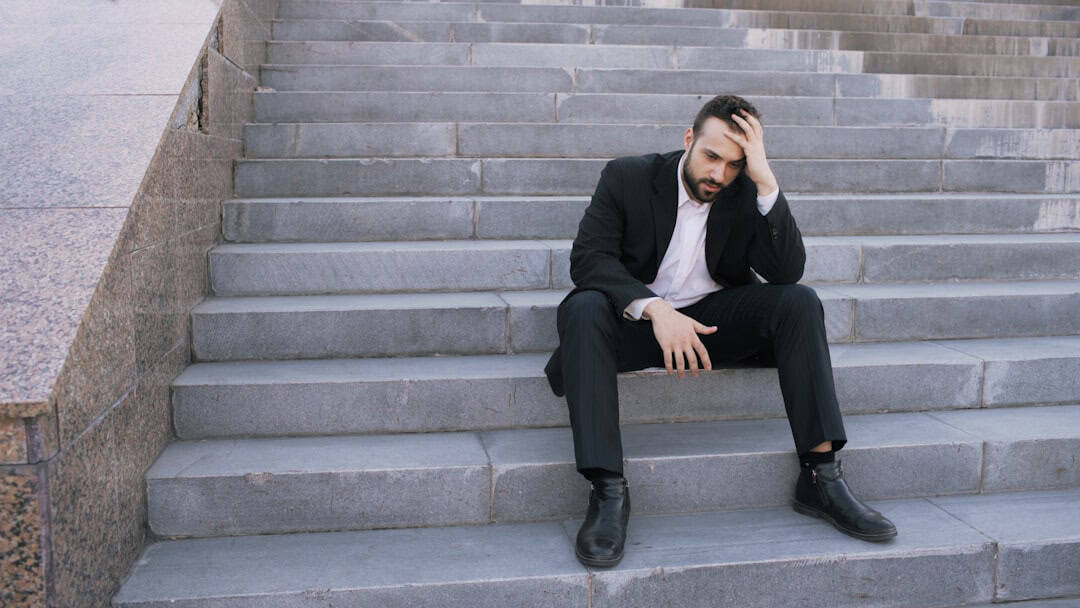 Frustrated man sitting on stairs in business attire, feeling stressed or overwhelmed.